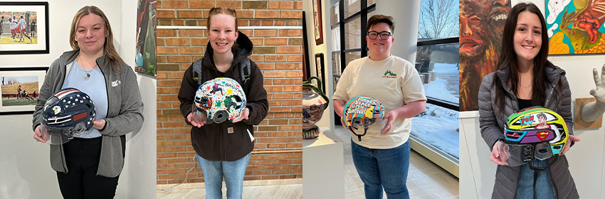 4 of 9 students who participated in the helmet painting event all holding their helmests in front of their art work in the student art show